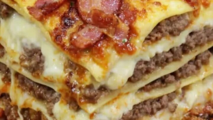 A towering square slice of garlic parmesan bacon lasagna served on a rustic wooden board