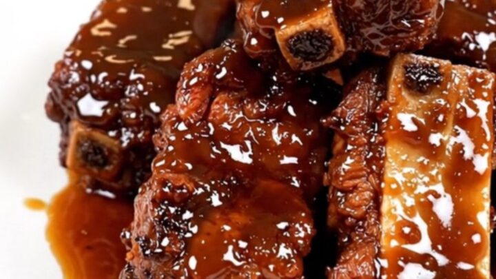 A top-down view of tender, glossy beef short ribs in a black slow cooker with green onion garnish.