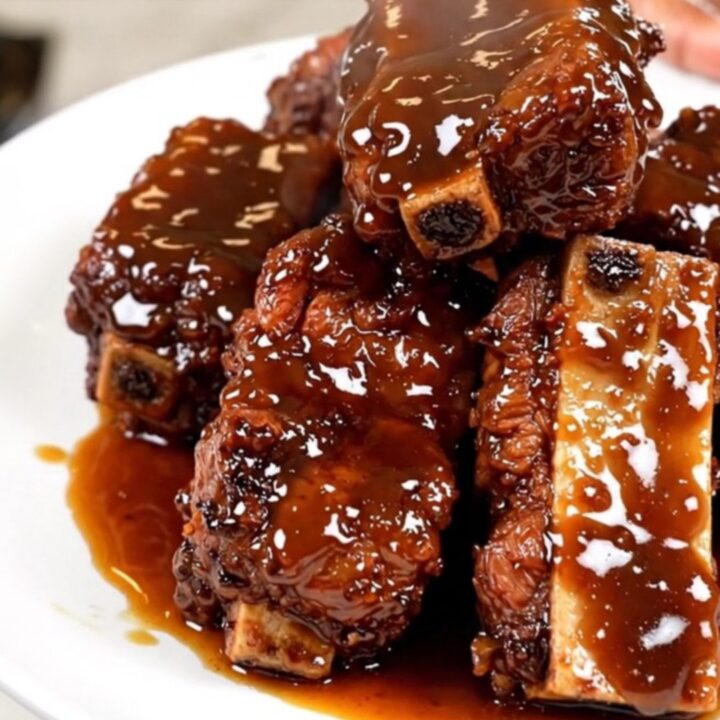 A top-down view of tender, glossy beef short ribs in a black slow cooker with green onion garnish.
