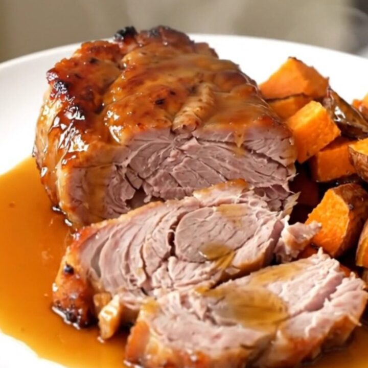 A close-up of glazed pork tenderloin and sweet potatoes served on a white plate.