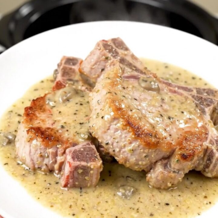 A close-up of tender, slow-cooked pork chops smothered in a creamy, glossy garlic parmesan sauce.
