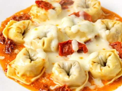 A close-up of creamy sun-dried tomato tortellini in a slow cooker with steam rising.