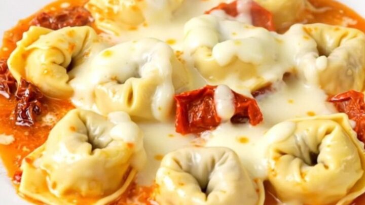 A close-up of creamy sun-dried tomato tortellini in a slow cooker with steam rising.
