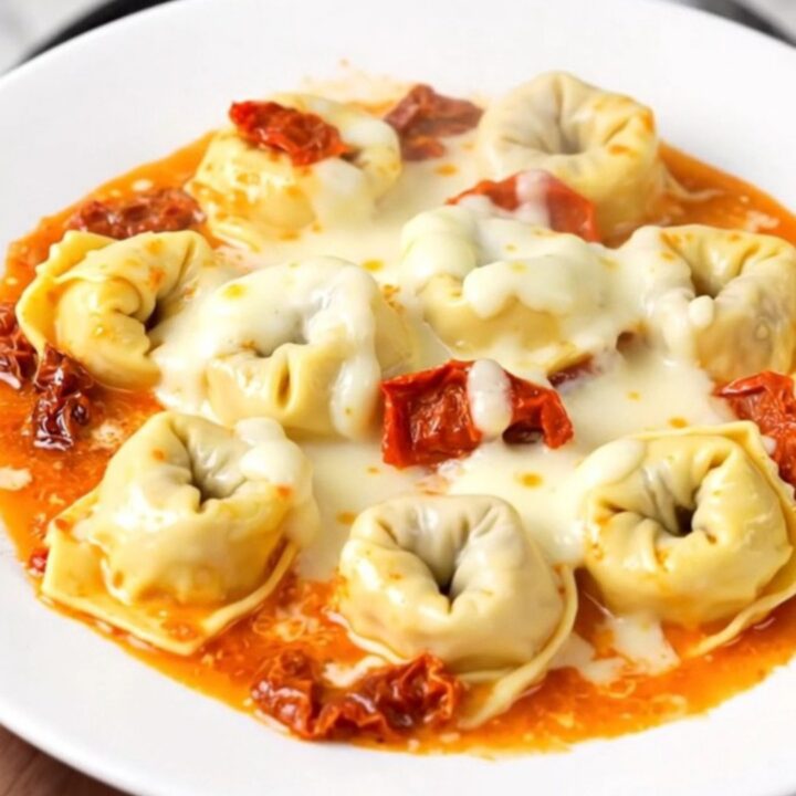 A close-up of creamy sun-dried tomato tortellini in a slow cooker with steam rising.