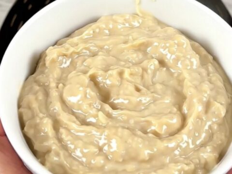 A warm, glossy crab rangoon dip in a white bowl, steaming slightly with green onions on top.