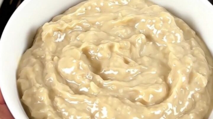 A warm, glossy crab rangoon dip in a white bowl, steaming slightly with green onions on top.