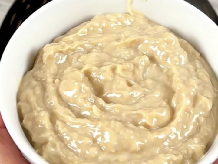 A warm, glossy crab rangoon dip in a white bowl, steaming slightly with green onions on top.