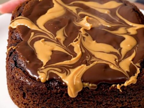 A close-up of a warm, gooey chocolate and peanut butter dump cake served in a white bowl.