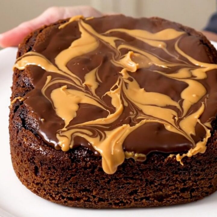 A close-up of a warm, gooey chocolate and peanut butter dump cake served in a white bowl.