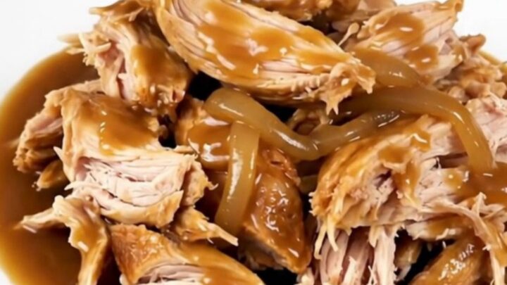 A whole chicken cooked in a slow cooker, surrounded by rich, caramelized onions and a glossy, dark gravy.