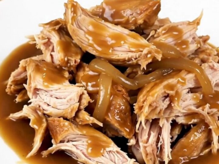A whole chicken cooked in a slow cooker, surrounded by rich, caramelized onions and a glossy, dark gravy.