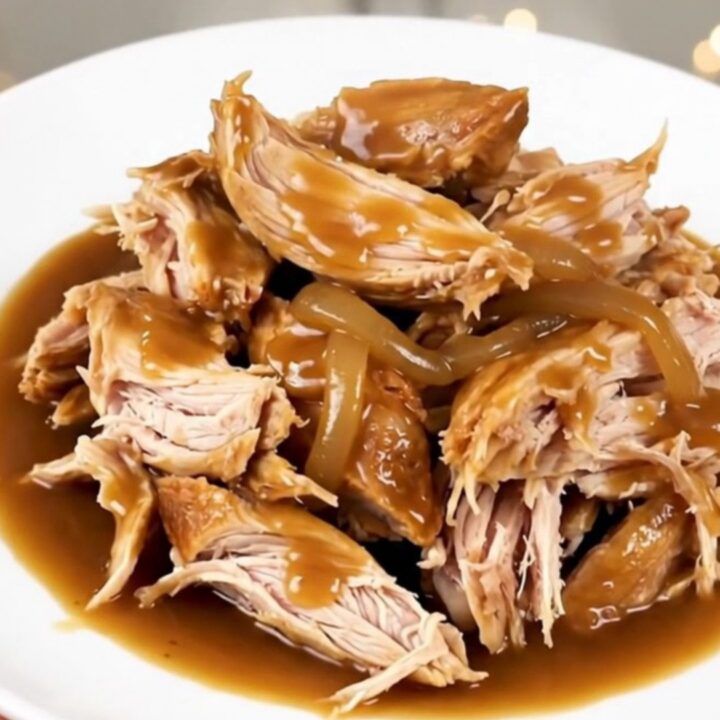 A whole chicken cooked in a slow cooker, surrounded by rich, caramelized onions and a glossy, dark gravy.