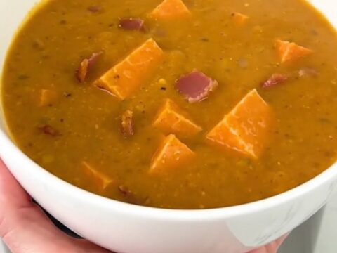 A close-up of creamy pumpkin bacon chowder in a white bowl with visible bacon bits.