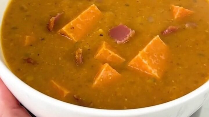 A close-up of creamy pumpkin bacon chowder in a white bowl with visible bacon bits.