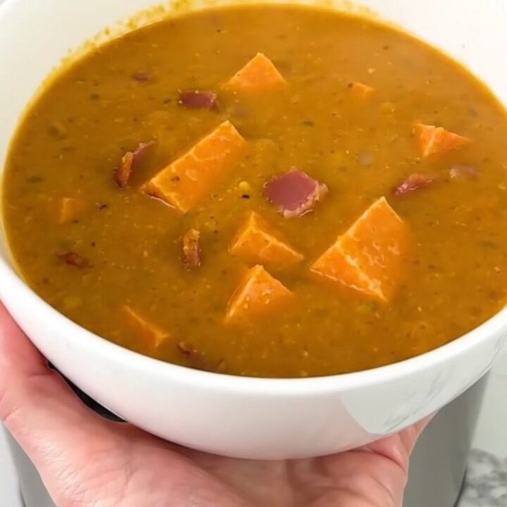 A close-up of creamy pumpkin bacon chowder in a white bowl with visible bacon bits.