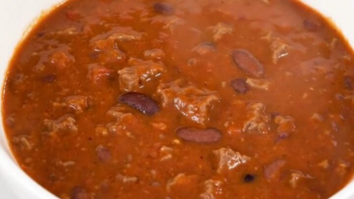 A steaming bowl of smoky chipotle beef chili in a white bowl on a kitchen counter.