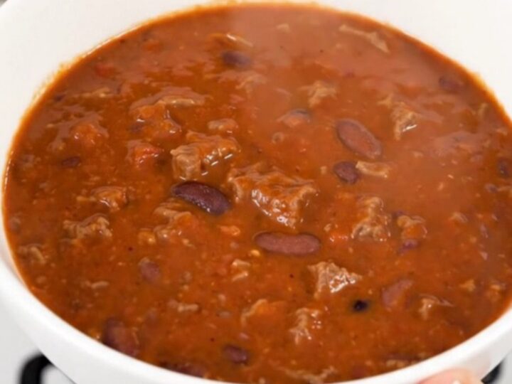 A steaming bowl of smoky chipotle beef chili in a white bowl on a kitchen counter.