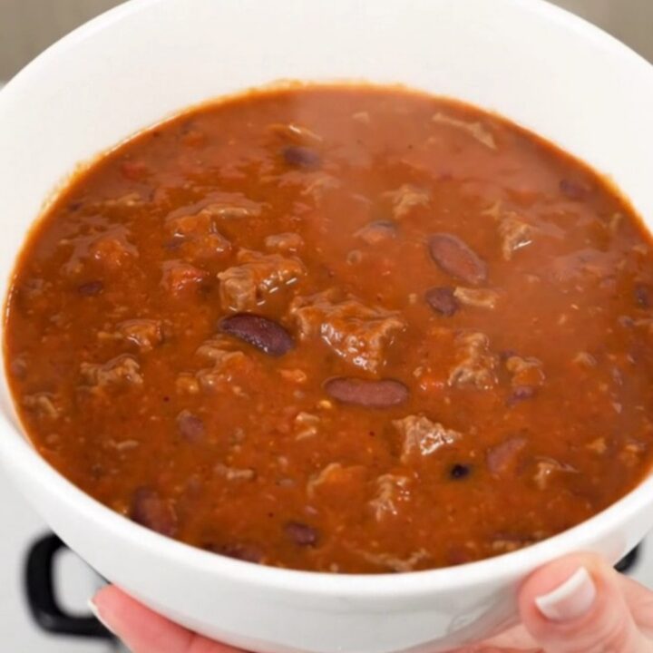 A steaming bowl of smoky chipotle beef chili in a white bowl on a kitchen counter.