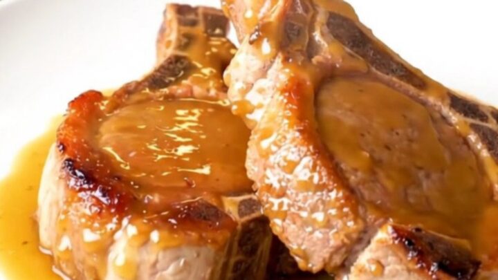 Close-up of tender glazed pork chops on a white plate with a glossy brown sugar and Dijon sauce.