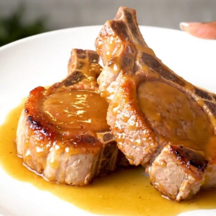 Close-up of tender glazed pork chops on a white plate with a glossy brown sugar and Dijon sauce.