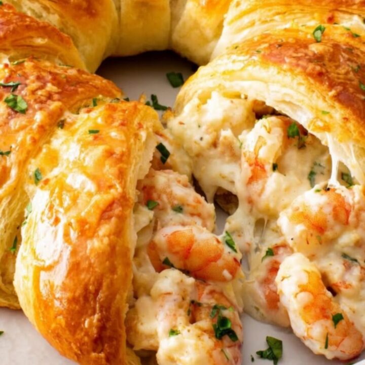 A golden-brown seafood crescent ring sliced open to reveal steaming melted cheese, tender pink shrimp