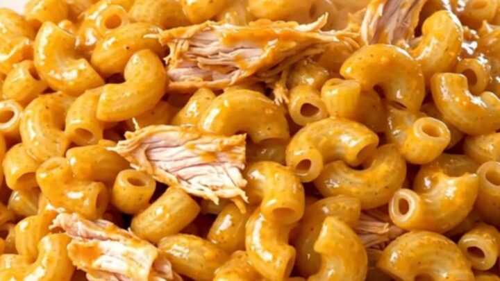 A top-down view of raw chicken, cream cheese, and sauce being added to a black slow cooker.