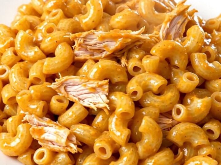 A top-down view of raw chicken, cream cheese, and sauce being added to a black slow cooker.