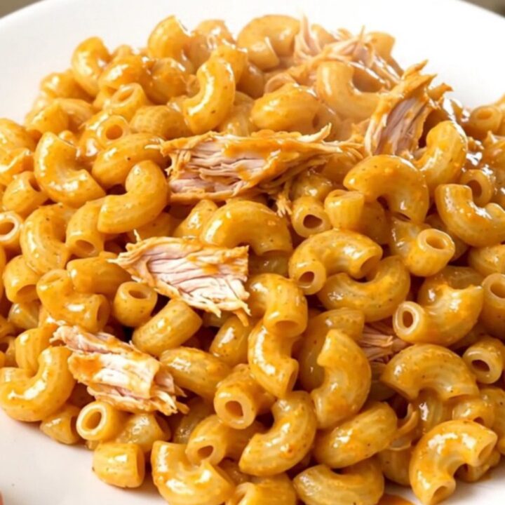 A top-down view of raw chicken, cream cheese, and sauce being added to a black slow cooker.