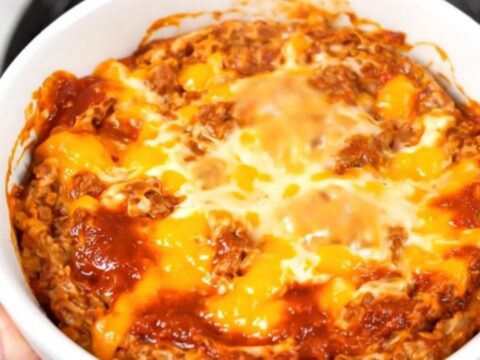 A top-down view of a steaming, creamy chorizo dip in a black slow cooker on a white quartz countertop.