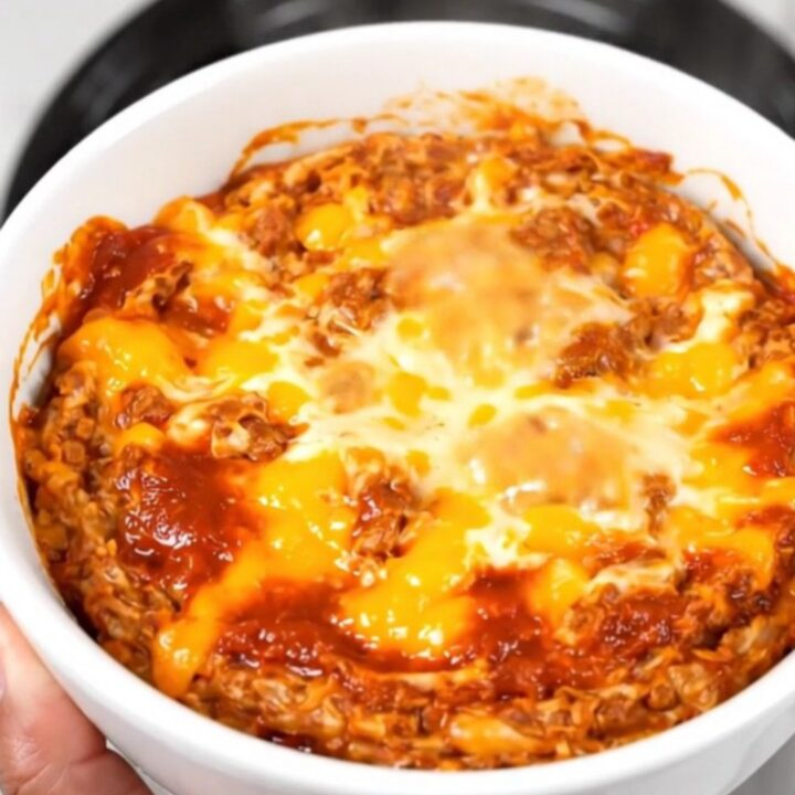 A top-down view of a steaming, creamy chorizo dip in a black slow cooker on a white quartz countertop.