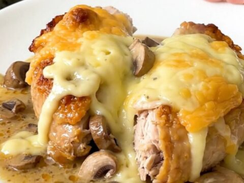 A slow cooker filled with chicken breasts, sliced mushrooms, and a creamy sauce.