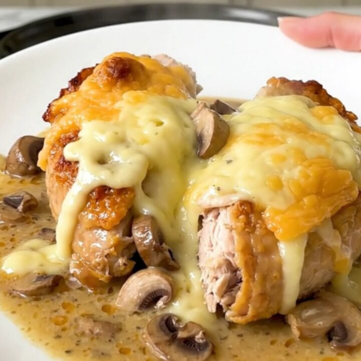 A slow cooker filled with chicken breasts, sliced mushrooms, and a creamy sauce.