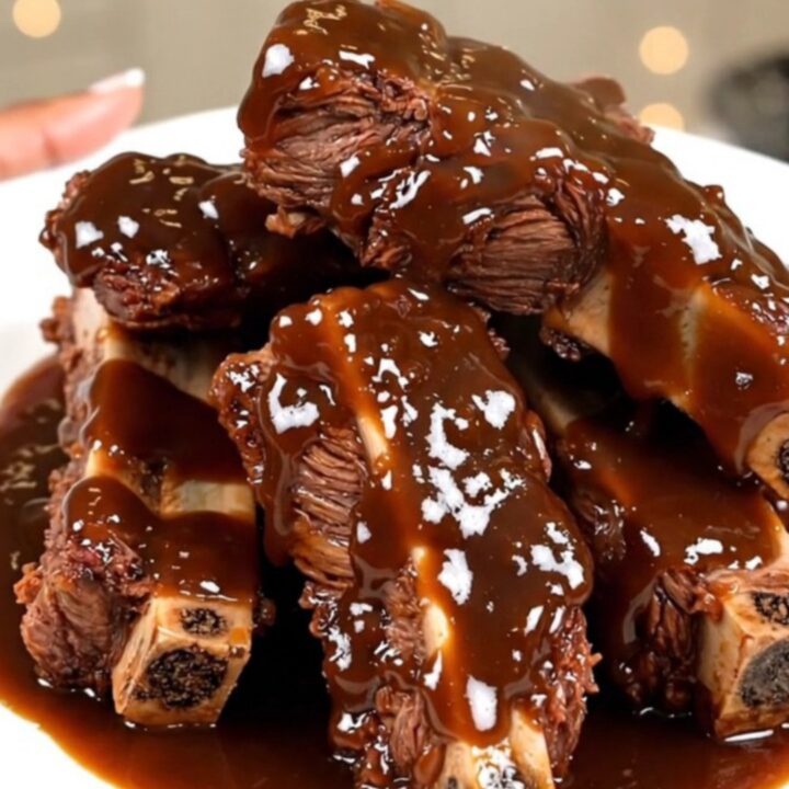 A close-up of tender, glistening beef short ribs covered in a rich bourbon barbecue sauce on a white plate.