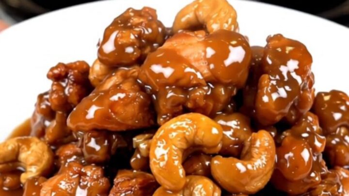 A close-up of glossy cashew chicken in a slow cooker with visible cashews and a rich sauce.