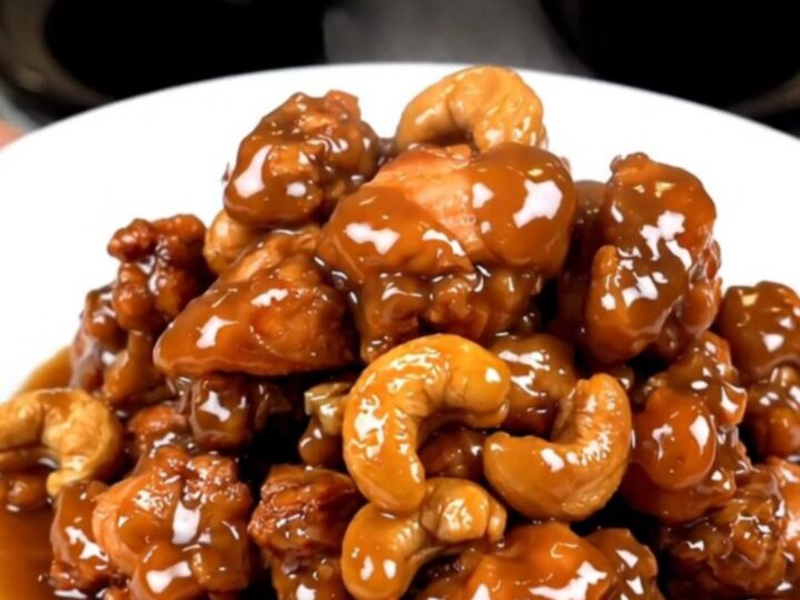 A close-up of glossy cashew chicken in a slow cooker with visible cashews and a rich sauce.