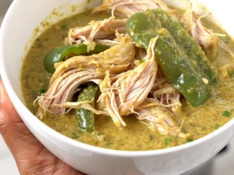 A top-down view of a slow cooker filled with chicken thighs, chopped poblano peppers, and a block of cream cheese.