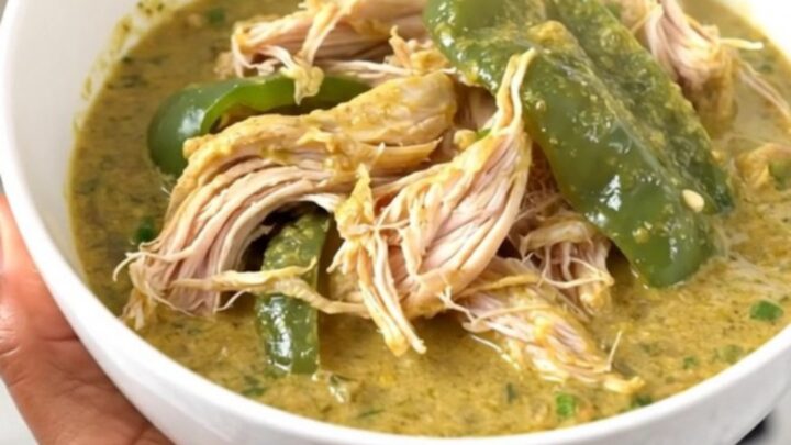 A top-down view of a slow cooker filled with chicken thighs, chopped poblano peppers, and a block of cream cheese.