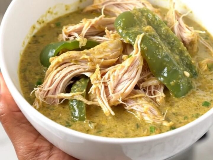 A top-down view of a slow cooker filled with chicken thighs, chopped poblano peppers, and a block of cream cheese.