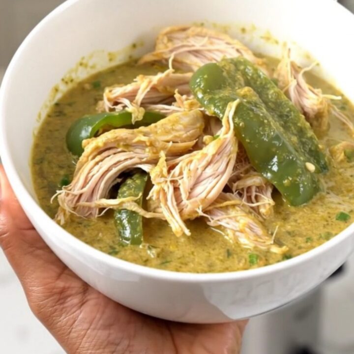 A top-down view of a slow cooker filled with chicken thighs, chopped poblano peppers, and a block of cream cheese.