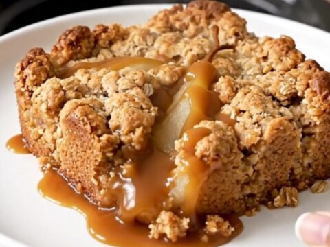 A warm, golden caramel pear crisp served in a white bowl with a spoon, highlighting the bubbly sauce and tender pears.