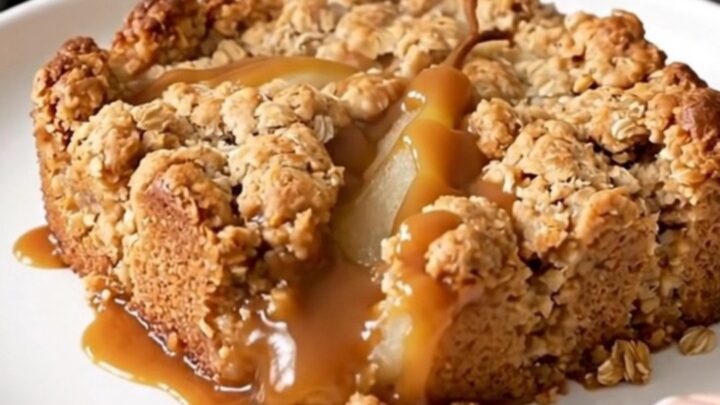 A warm, golden caramel pear crisp served in a white bowl with a spoon, highlighting the bubbly sauce and tender pears.