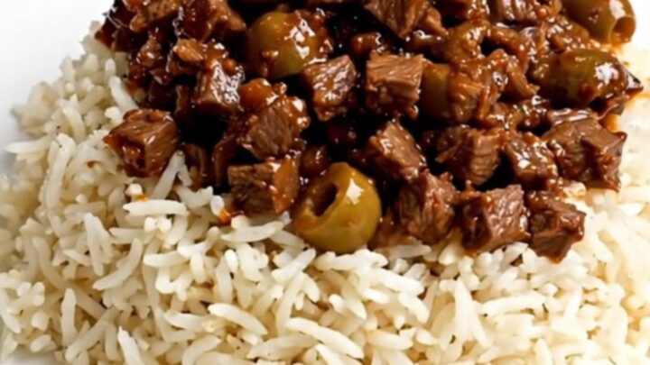 A close-up of a steaming bowl of beef picadillo served over fluffy white rice on a clean white plate.
