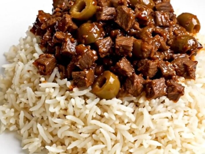 A close-up of a steaming bowl of beef picadillo served over fluffy white rice on a clean white plate.