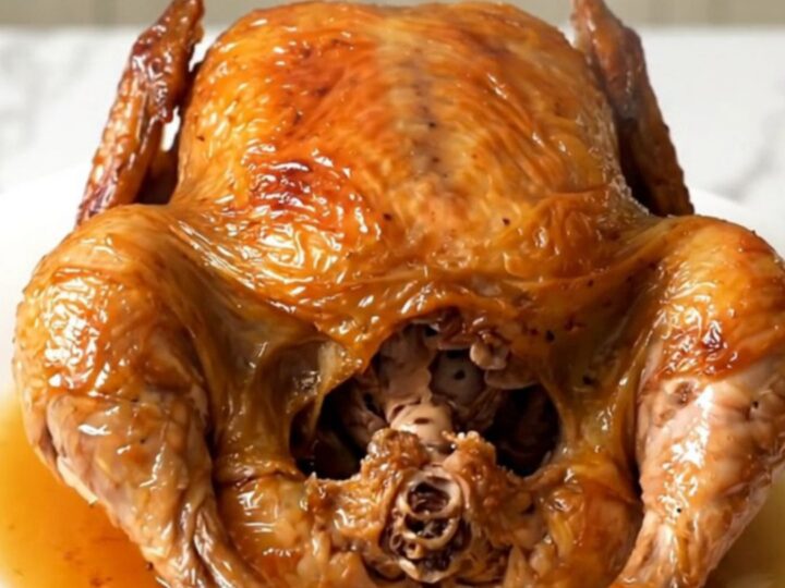 A golden, tender whole chicken cooked in a slow cooker, served on a white plate.