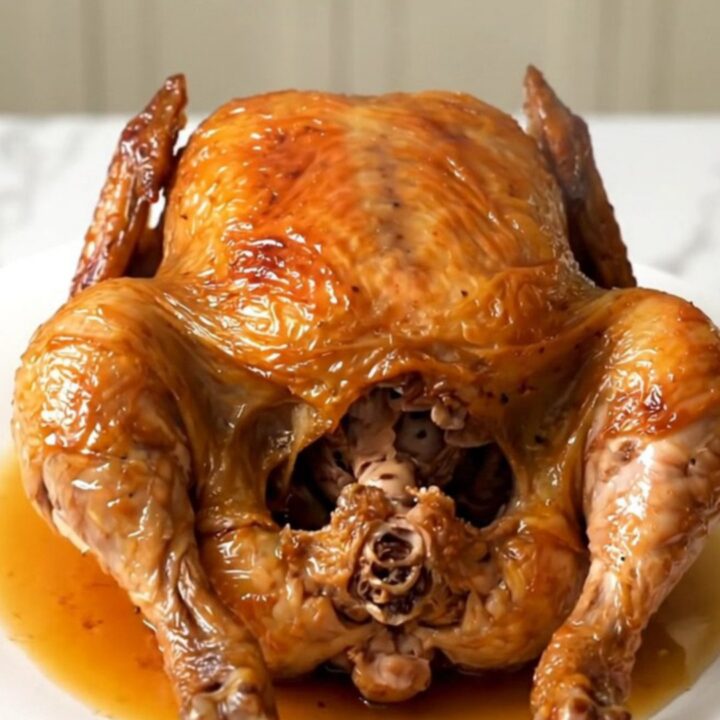 A golden, tender whole chicken cooked in a slow cooker, served on a white plate.