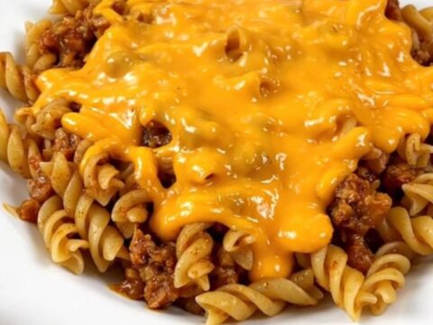 A close-up of a white plate filled with cheesy beef fiesta pasta, featuring visible ground beef, rotini