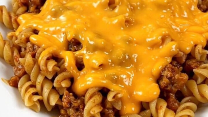 A close-up of a white plate filled with cheesy beef fiesta pasta, featuring visible ground beef, rotini