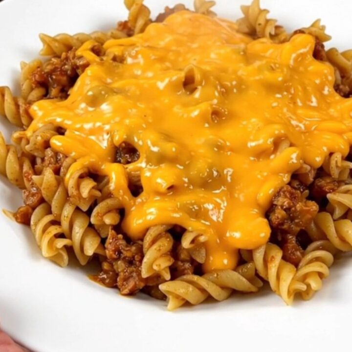 A close-up of a white plate filled with cheesy beef fiesta pasta, featuring visible ground beef, rotini