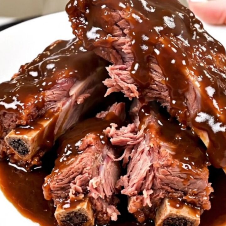 A top-down view of raw beef short ribs, chopped red onion, and barbecue sauce inside a black slow cooker.