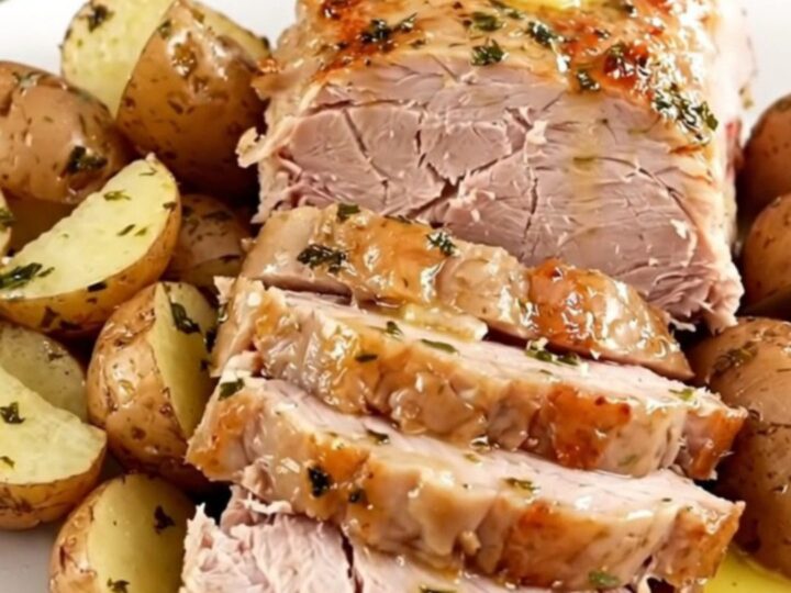 A close-up of a tender, sliced pork loin roast and buttery baby red potatoes on a white plate.